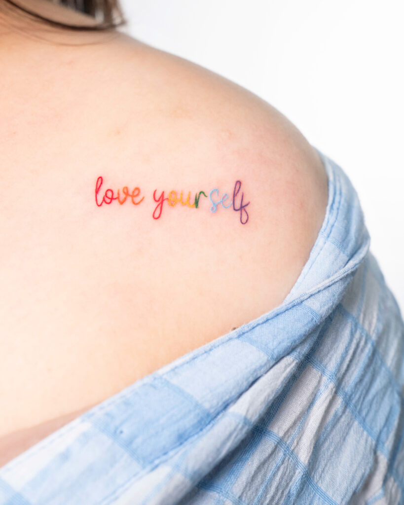 Colourful tattoo saying 'love yourself', rainbow text tattoo.