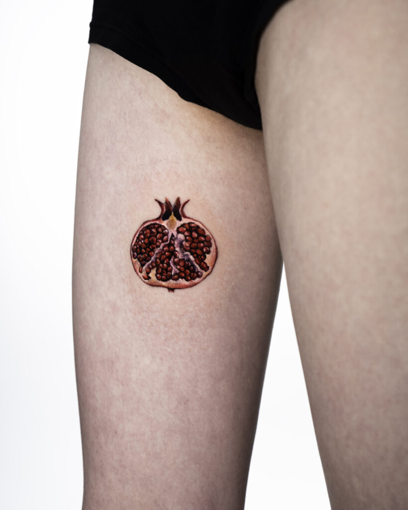 Realistic pomegranate tattoo on thigh.
