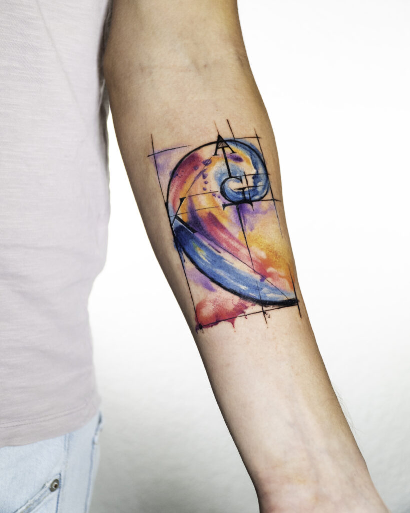 Abstract Geometrical Watercolor Tattoo placed on inner side of the front arm. Main colors are pink, blue and yellow.