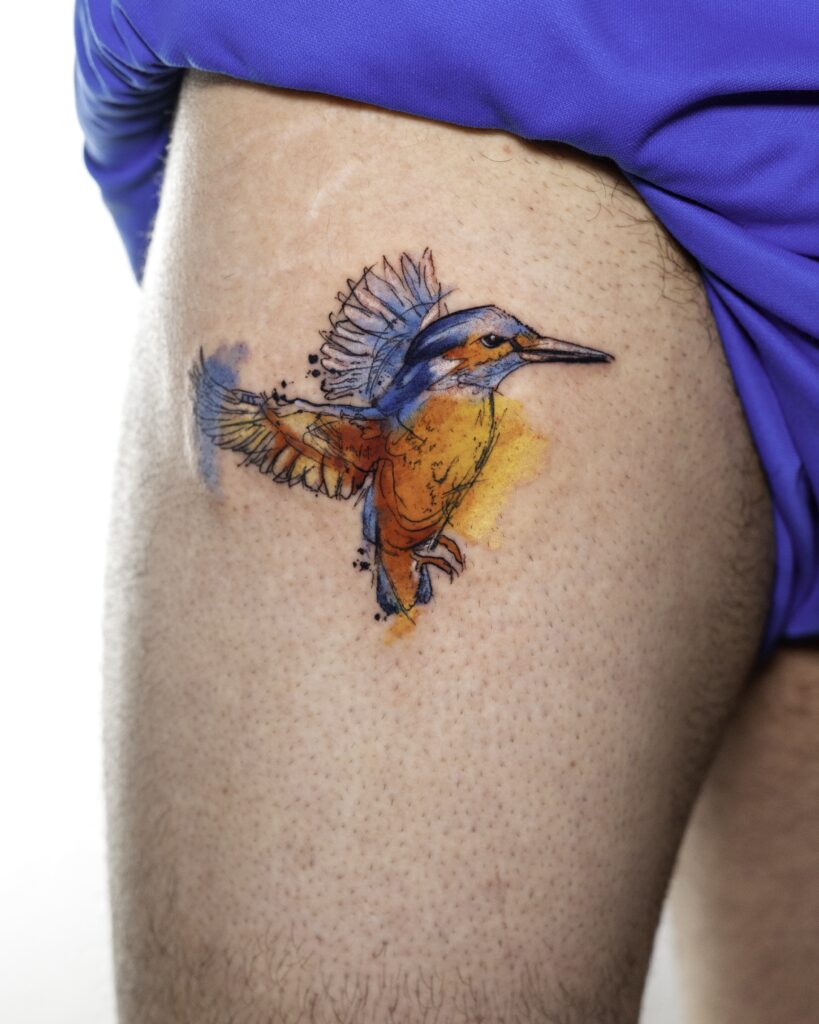 Watercolor Hummingbird Tatoo on leg with orange, blue and yellow.